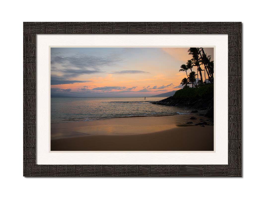 A photo looking out to sea at Maui during sunrise. A surfer can be seen on the water in the distance. Printed on paper, matted, and framed.