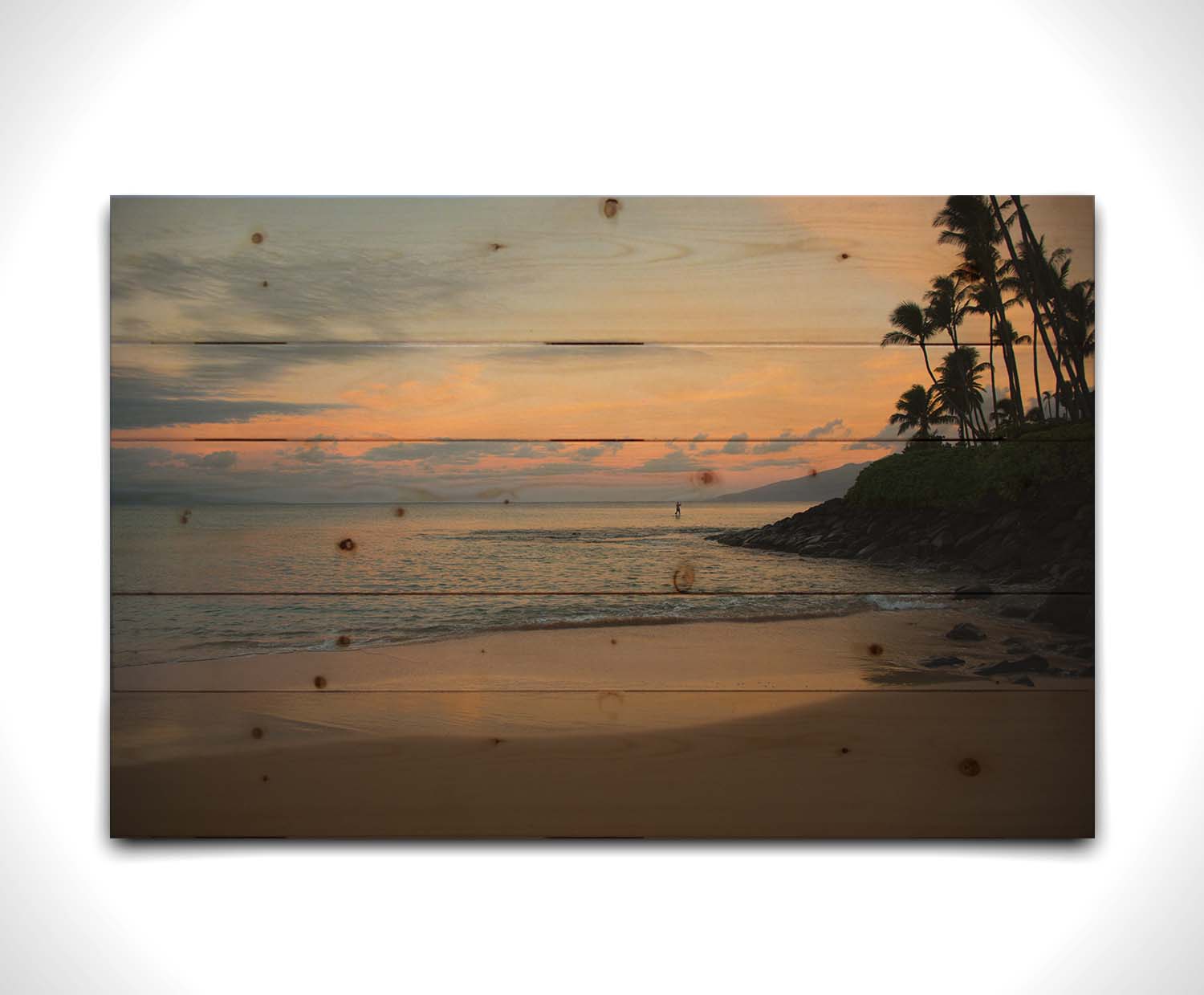 A photo looking out to sea at Maui during sunrise. A surfer can be seen on the water in the distance. Printed on a wood pallet.