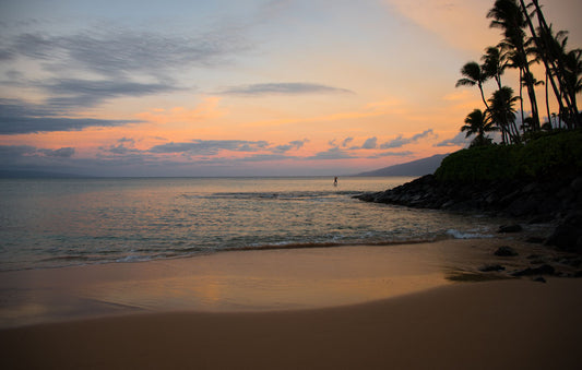 A photo looking out to sea at Maui during sunrise. A surfer can be seen on the water in the distance.