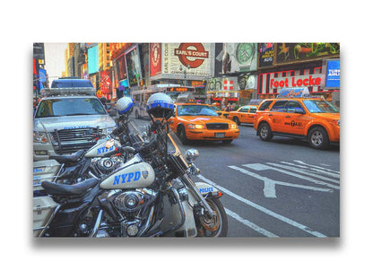 A photo of a street in New York City, featuring several bright orange taxis and New York Police Department vehicles. Printed on canvas.