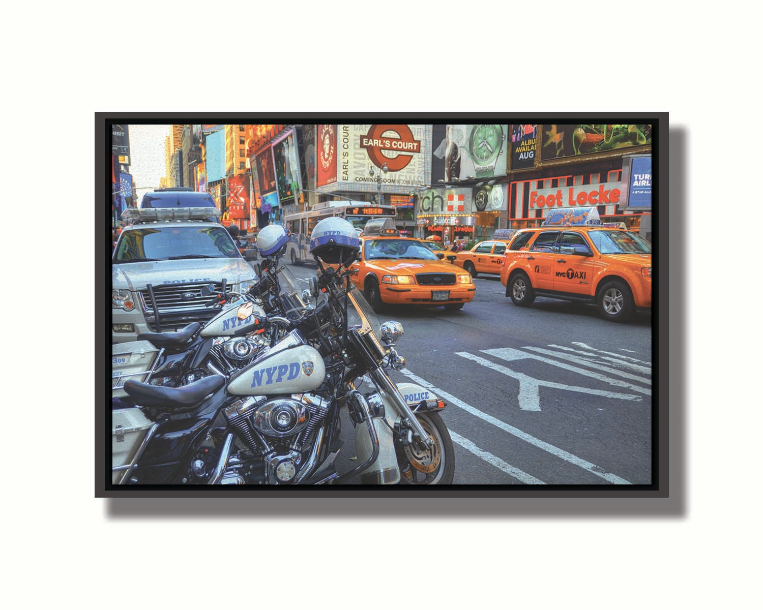 A photo of a street in New York City, featuring several bright orange taxis and New York Police Department vehicles. Printed on canvas in a float frame.