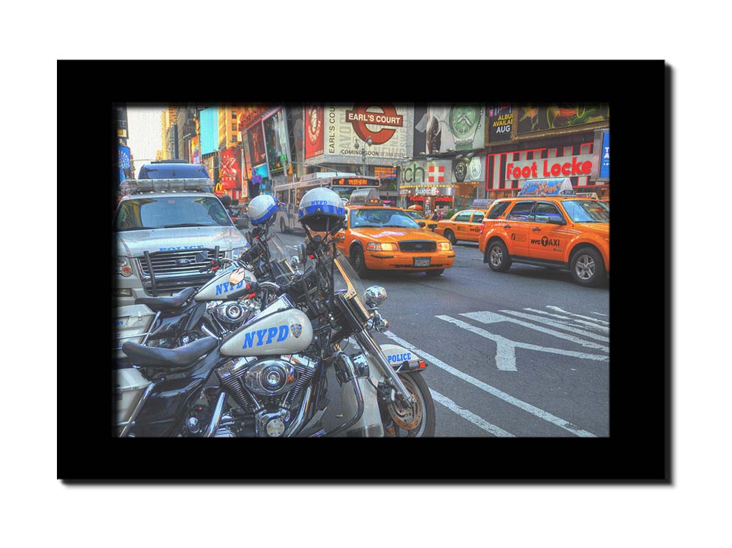 A photo of a street in New York City, featuring several bright orange taxis and New York Police Department vehicles. Printed on canvas and framed.