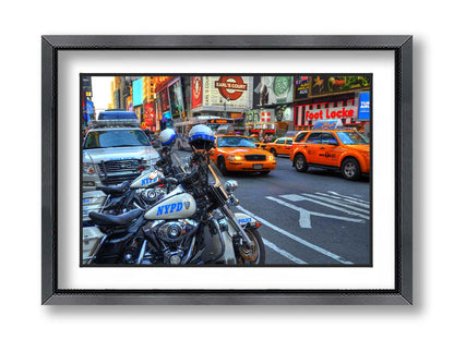 A photo of a street in New York City, featuring several bright orange taxis and New York Police Department vehicles. Printed on paper, matted, and framed.