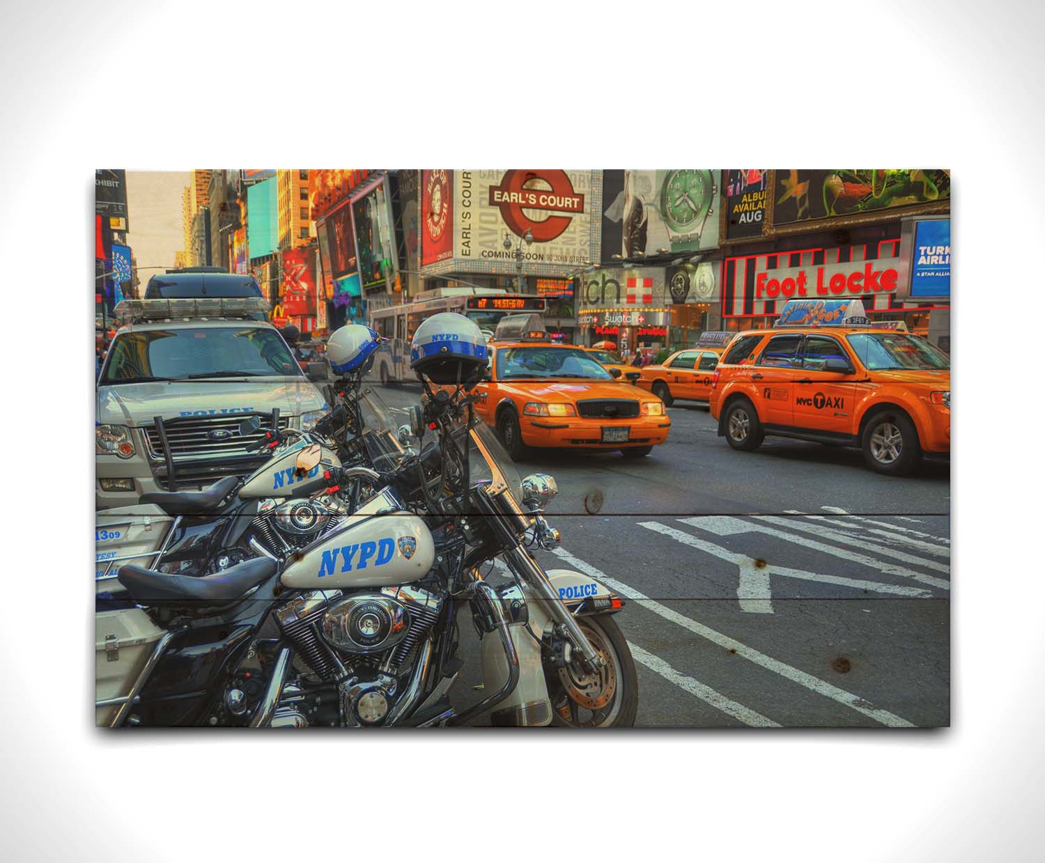 A photo of a street in New York City, featuring several bright orange taxis and New York Police Department vehicles. Printed on a wood pallet.