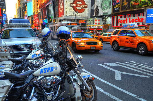 A photo of a street in New York City, featuring several bright orange taxis and New York Police Department vehicles.