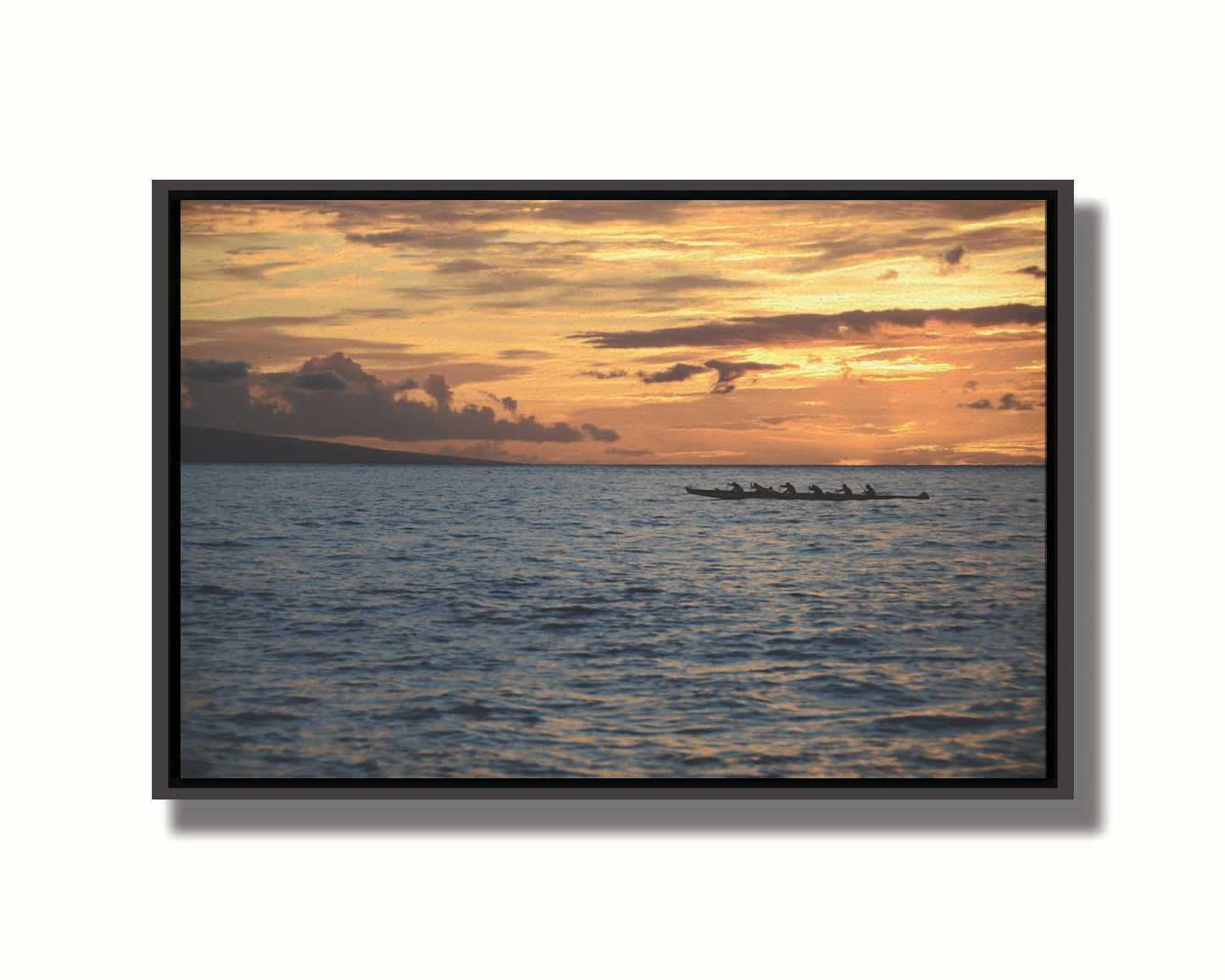 A photo of an outrigger canoe silhouetted on the sea by an orange sunset off the coat of Hawaiʻi. Printed on canvas in a float frame.