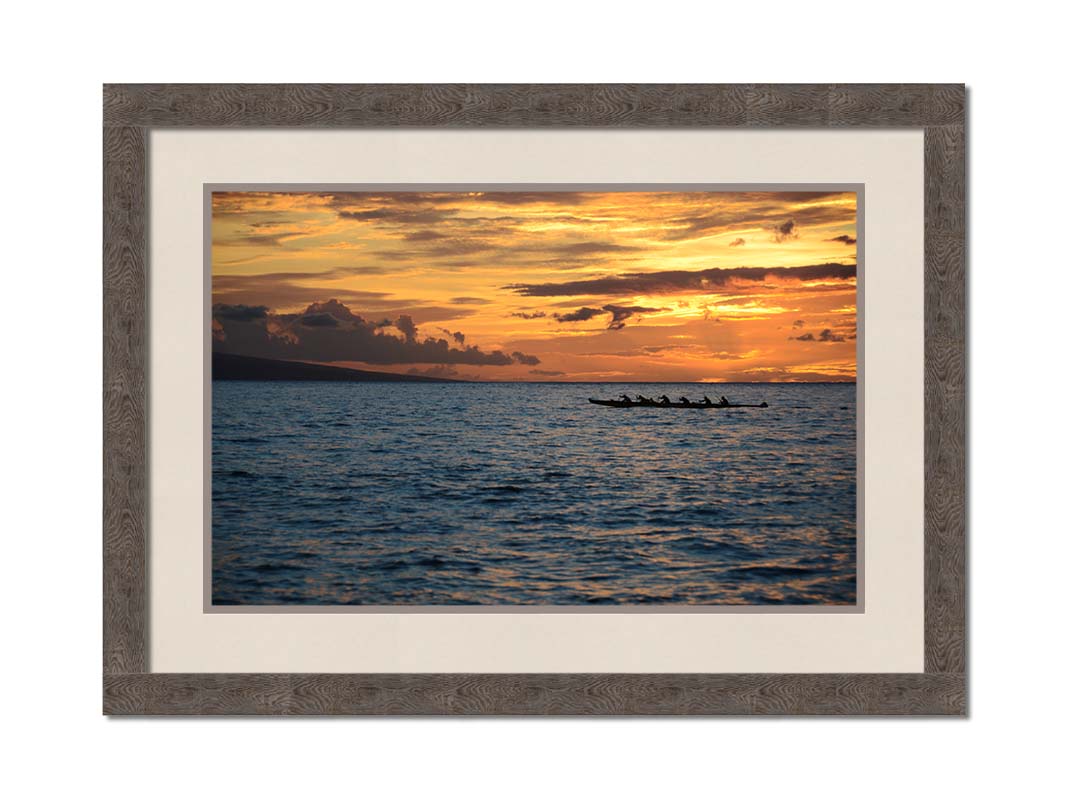 A photo of an outrigger canoe silhouetted on the sea by an orange sunset off the coat of Hawaiʻi. Printed on paper, matted, and framed.