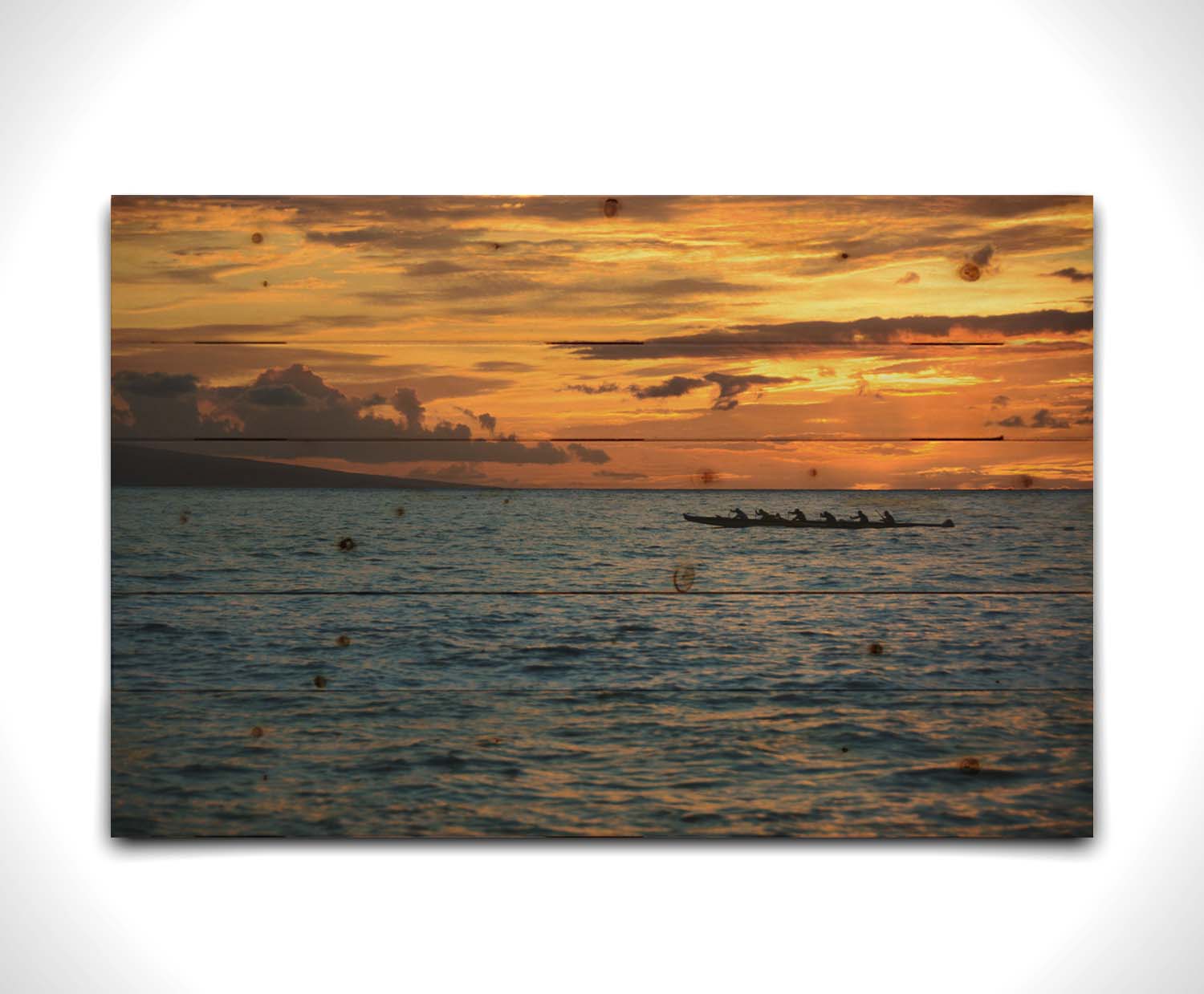 A photo of an outrigger canoe silhouetted on the sea by an orange sunset off the coat of Hawaiʻi. Printed on a wood pallet.