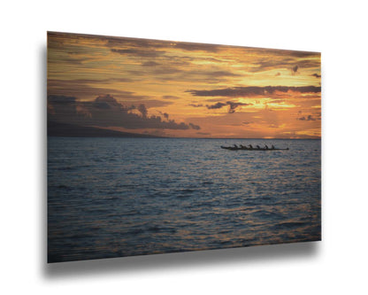 A photo of an outrigger canoe silhouetted on the sea by an orange sunset off the coat of Hawaiʻi. Printed on metal.