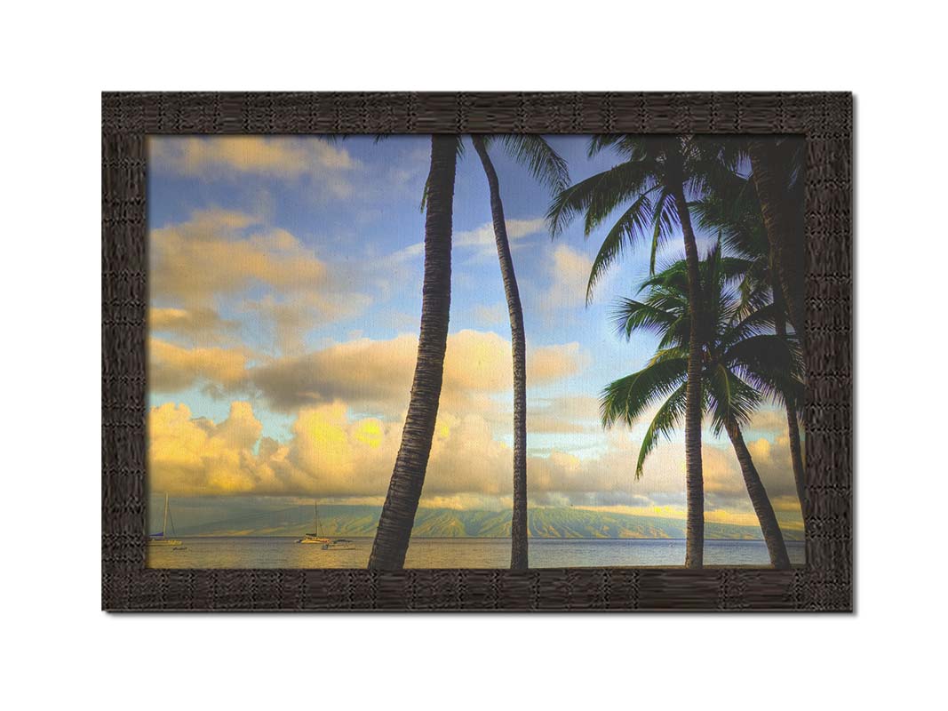 A photo of a collection of palm trees, backed by a view of the sea and distance mountainous islands lit with yellow from the low sun. Printed on canvas and framed.