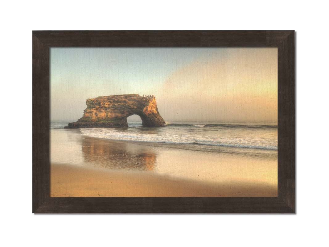 A photo of a "natural bridge" rock formation in Santa Cruz, California. A group of pelicans sit on top of the structure above the sea. Printed on canvas and framed.