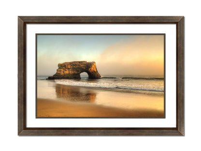 A photo of a "natural bridge" rock formation in Santa Cruz, California. A group of pelicans sit on top of the structure above the sea. Printed on paper, matted, and framed.