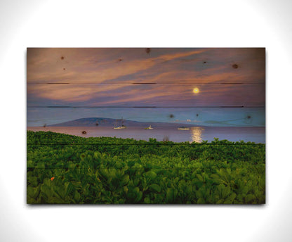 A photo overlooking the sea off the coast of Hawaiʻi as the moon sets. The foreground is filled with greenery, and ships can be seen sailing on the waters with mountains in the distance. Printed on a wood pallet.