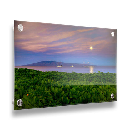 A photo overlooking the sea off the coast of Hawaiʻi as the moon sets. The foreground is filled with greenery, and ships can be seen sailing on the waters with mountains in the distance. Printed on acrylic.