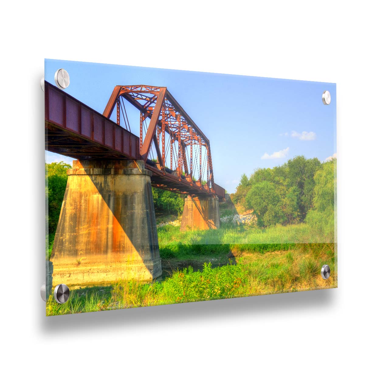 A photograph of a red metal bridge supported by concrete pillars, passing ove a grassy landscape on a clear day. Printed on acrylic.