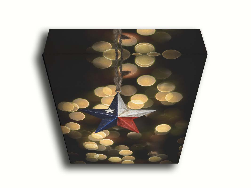 A photo of a christmas ornament of a star painted like the Texas state flag, with yellow bokeh in the background. Printed on canvas.