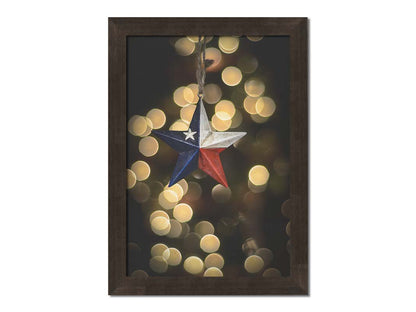 A photo of a christmas ornament of a star painted like the Texas state flag, with yellow bokeh in the background. Printed on canvas and framed.