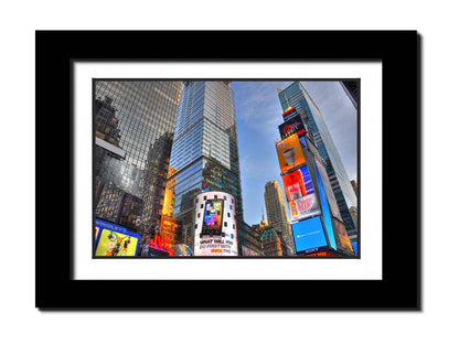 A photo looking up at the buildings and advertisements of Times Square in New York. Printed on paper, matted, and framed.