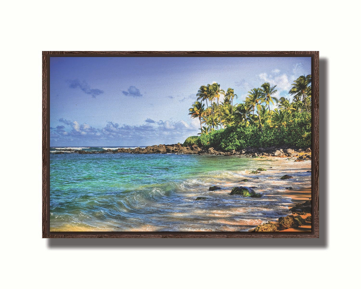 A photo of Laniākea beach. The water is a vibrant blue-green, and the stony beach circles around in the background where lush foliage and palm trees grow under a bright blue sky. Printed on canvas in a float frame.