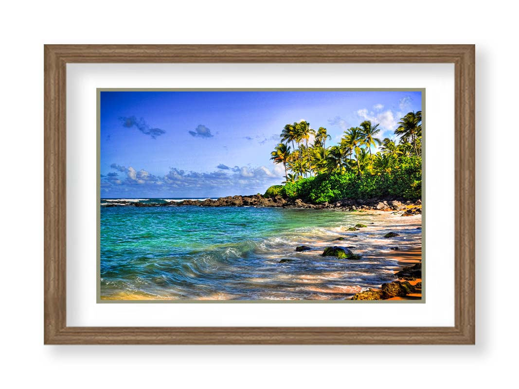 A photo of Laniākea beach. The water is a vibrant blue-green, and the stony beach circles around in the background where lush foliage and palm trees grow under a bright blue sky. Printed on paper, matted, and framed.