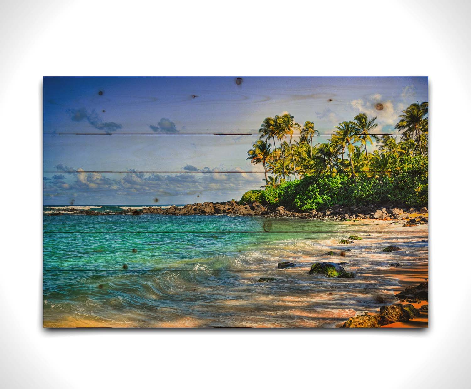 A photo of Laniākea beach. The water is a vibrant blue-green, and the stony beach circles around in the background where lush foliage and palm trees grow under a bright blue sky. Printed on a wood pallet.