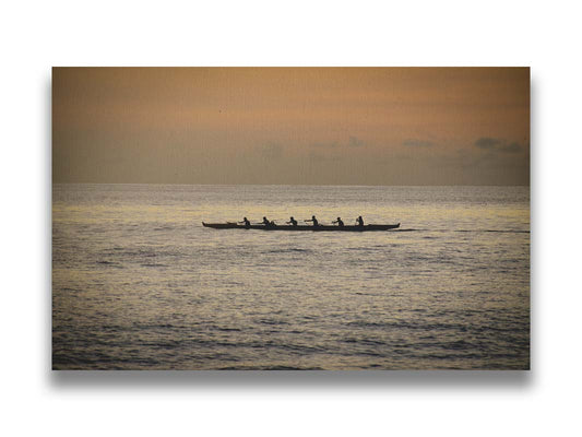 A photo of an outrigger canoe at sea, silhouetted against an orange sky. Printed on canvas.