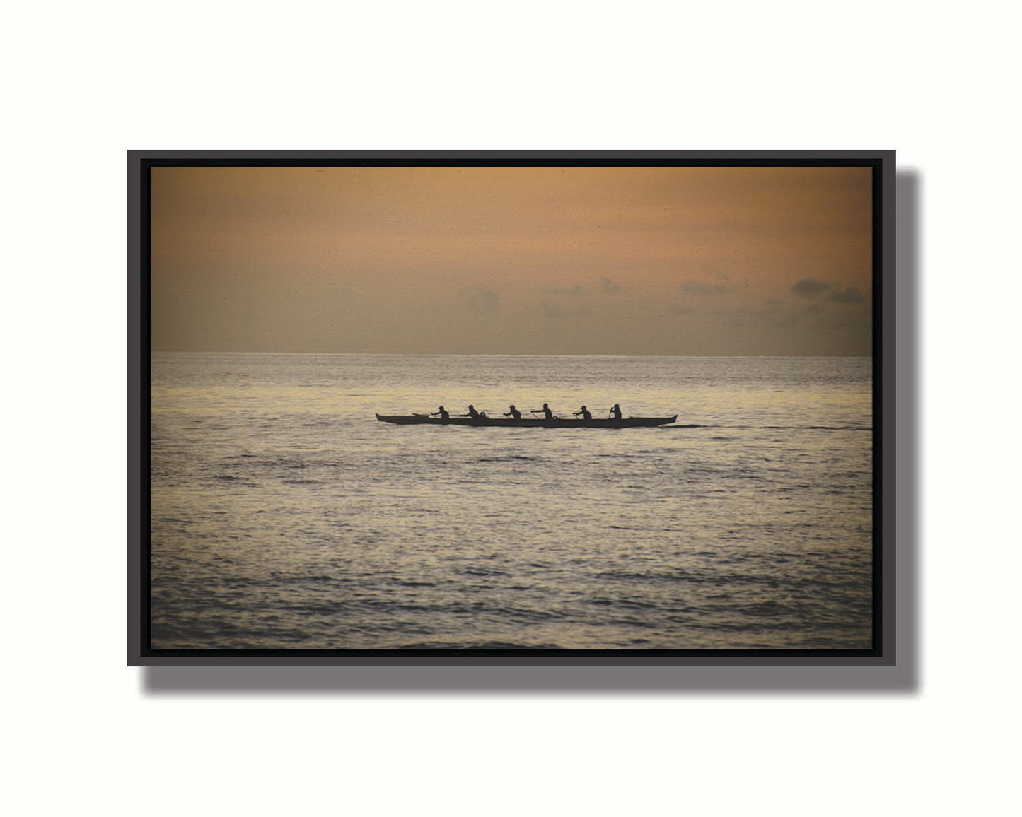 A photo of an outrigger canoe at sea, silhouetted against an orange sky. Printed on canvas in a float frame.