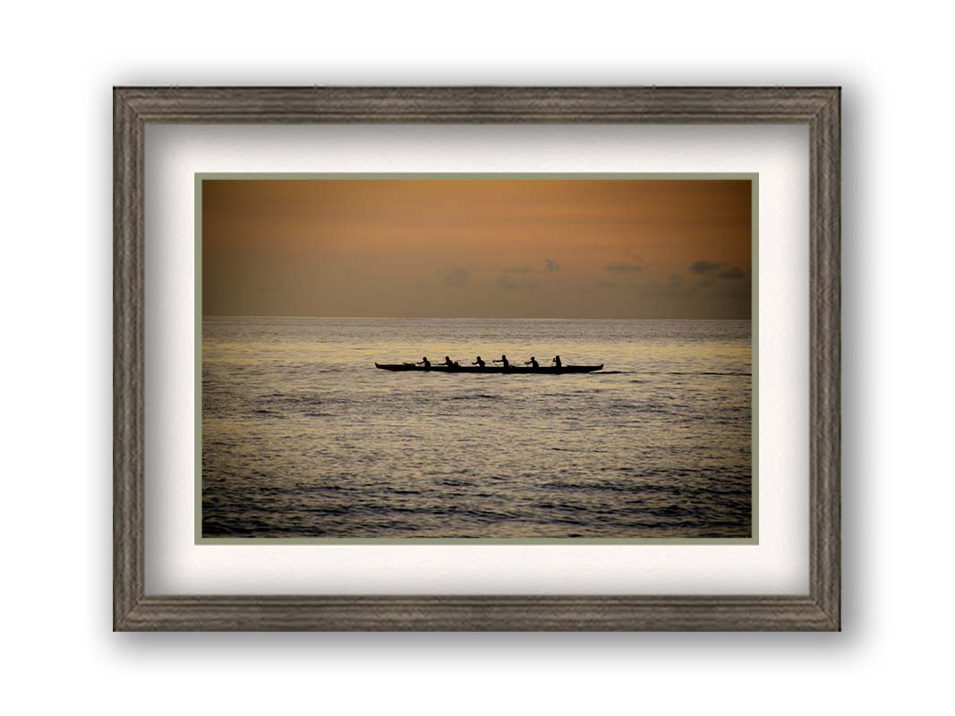 A photo of an outrigger canoe at sea, silhouetted against an orange sky. Printed on paper, matted, and framed.