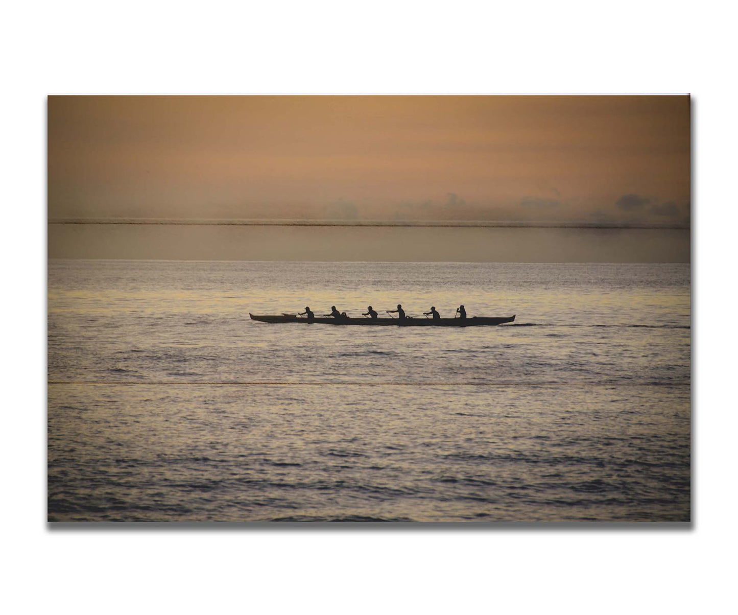 A photo of an outrigger canoe at sea, silhouetted against an orange sky. Printed on a box board.