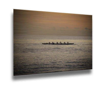 A photo of an outrigger canoe at sea, silhouetted against an orange sky. Printed on metal.