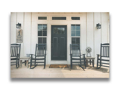 A photo of the door and front porch of a white house, with four black rocking chairs and a black door. Printed on canvas.