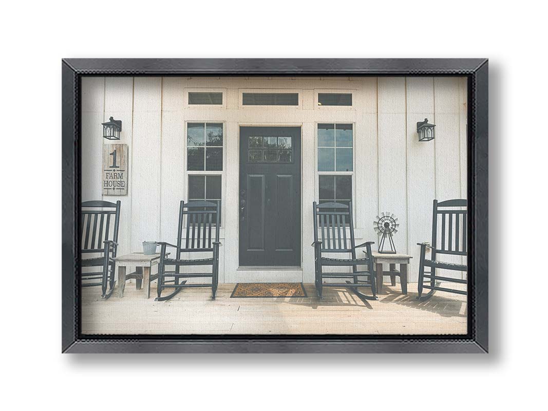 A photo of the door and front porch of a white house, with four black rocking chairs and a black door. Printed on canvas and framed.