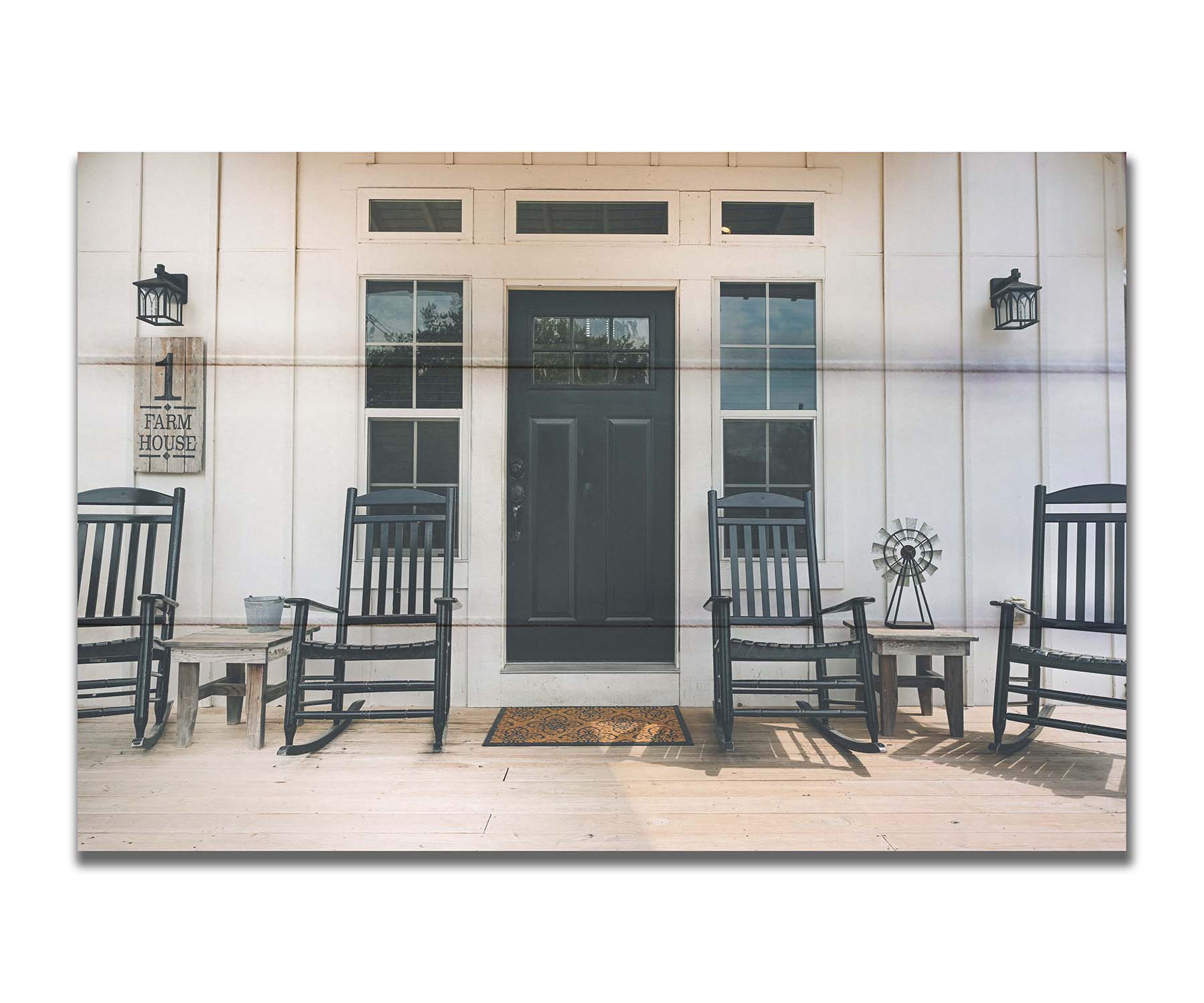 A photo of the door and front porch of a white house, with four black rocking chairs and a black door. Printed on a box board.