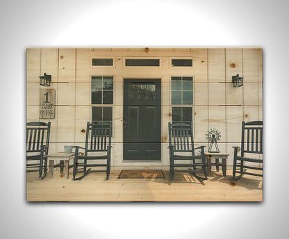 A photo of the door and front porch of a white house, with four black rocking chairs and a black door. Printed on a wood pallet.