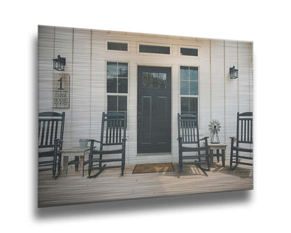 A photo of the door and front porch of a white house, with four black rocking chairs and a black door. Printed on metal.