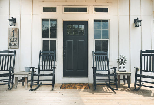 A photo of the door and front porch of a white house, with four black rocking chairs and a black door.