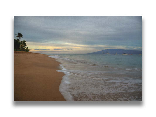 A photo of a cloudy sunrise on the Kaʻanapali shore, looking out to sea. Sailboats can be seen out on the water. Printed on canvas.