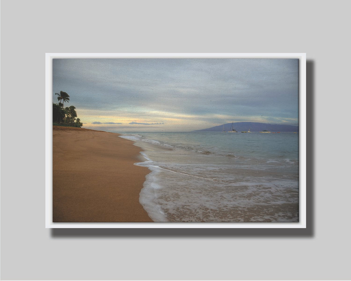 A photo of a cloudy sunrise on the Kaʻanapali shore, looking out to sea. Sailboats can be seen out on the water. Printed on canvas in a float frame.