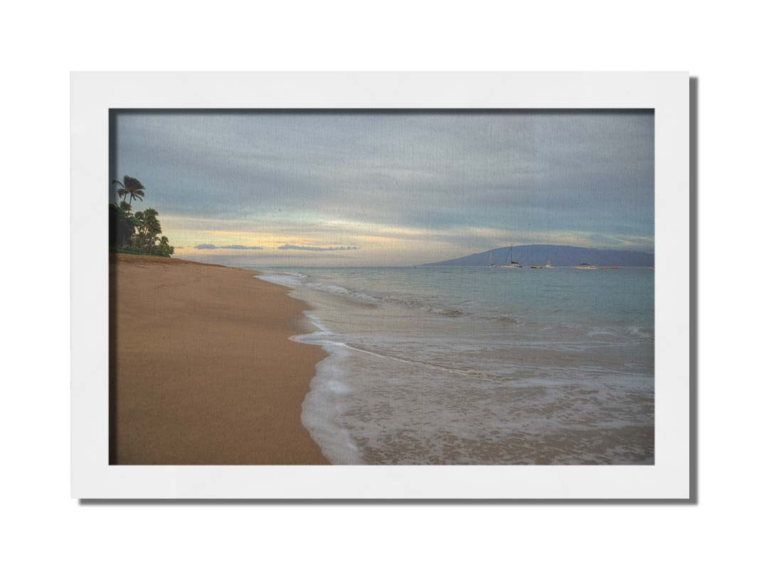 A photo of a cloudy sunrise on the Kaʻanapali shore, looking out to sea. Sailboats can be seen out on the water. Printed on canvas and framed.