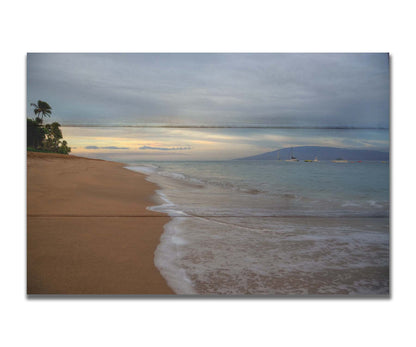 A photo of a cloudy sunrise on the Kaʻanapali shore, looking out to sea. Sailboats can be seen out on the water. Printed on a box board.