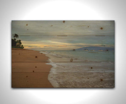 A photo of a cloudy sunrise on the Kaʻanapali shore, looking out to sea. Sailboats can be seen out on the water. Printed on a wood pallet.