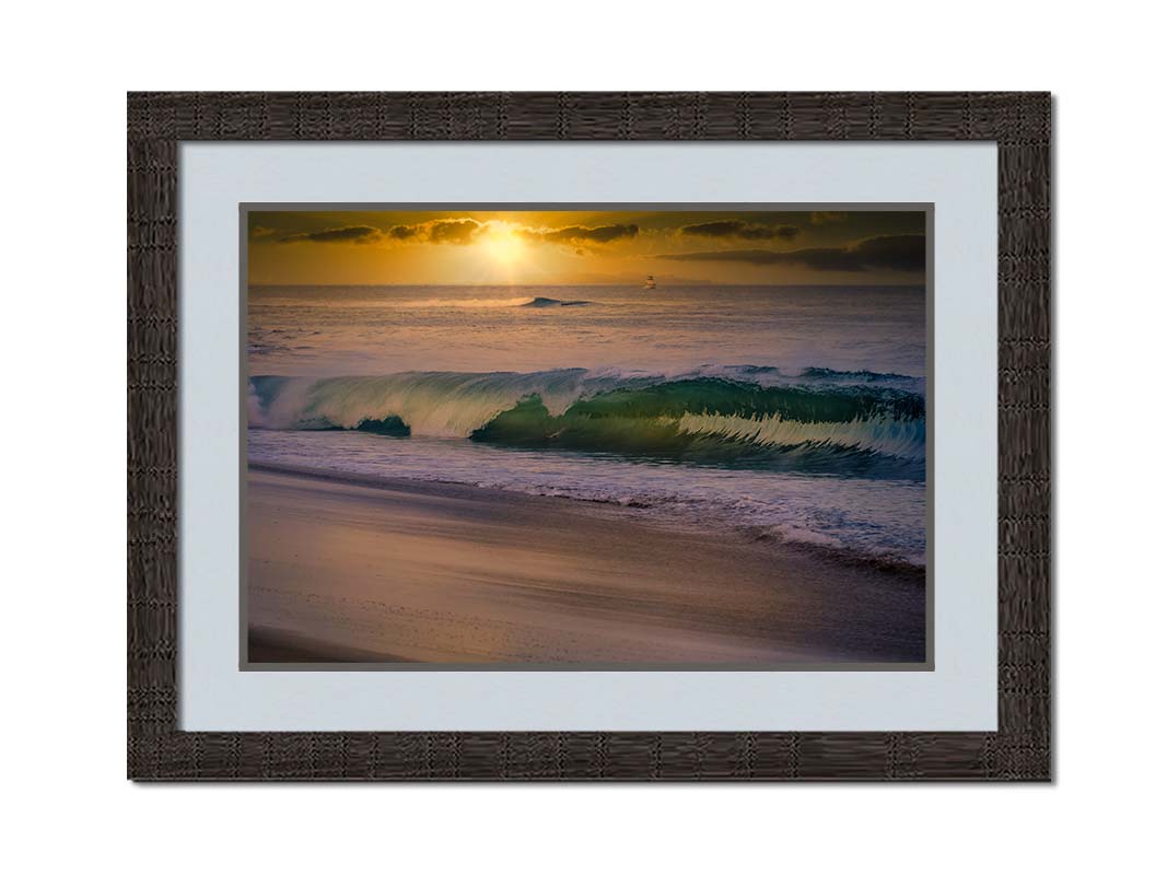 A photo of a calm sea wave rolling onto the beach on Maui at sunset. A boat can be seen on the water in the distance. Printed on paper, matted, and framed.