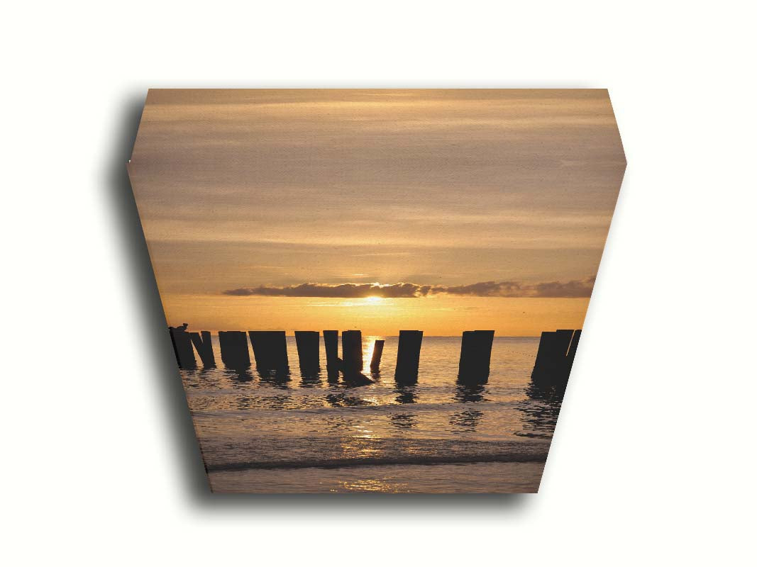 A photo of the remains of the Naples Beach pier in Florida. The sun is low on the horison and silhouettes the pillars in the sea. Printed on canvas.