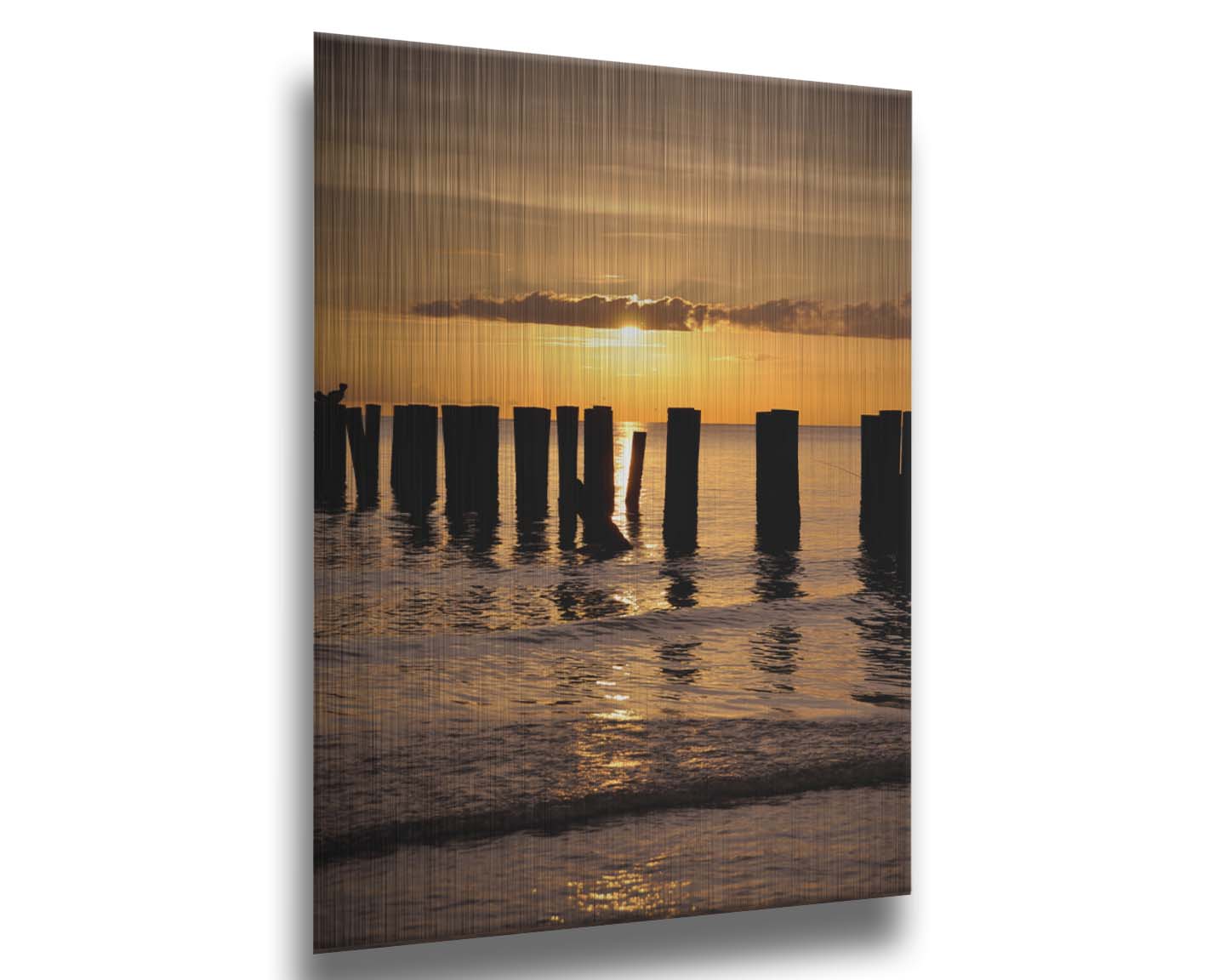 A photo of the remains of the Naples Beach pier in Florida. The sun is low on the horison and silhouettes the pillars in the sea. Printed on metal.