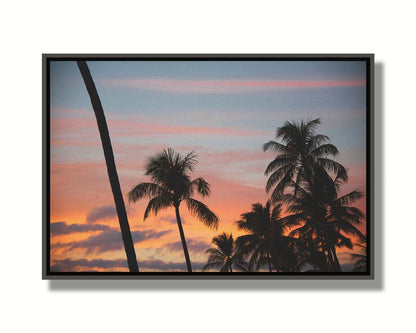 A photograph of Hawaiʻian palm trees, sihouetted against a sunset sky in orange, pink, and blue. Printed on canvas in a float frame.