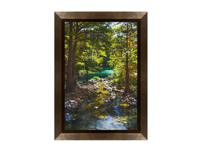 A photograph of the Guadalupe River in Gruene, Texas. Trees and foliage thrive around the water source, creating a lush green scene. The river reflects a vibrant turquoise behind the trees. Printed on canvas and framed.