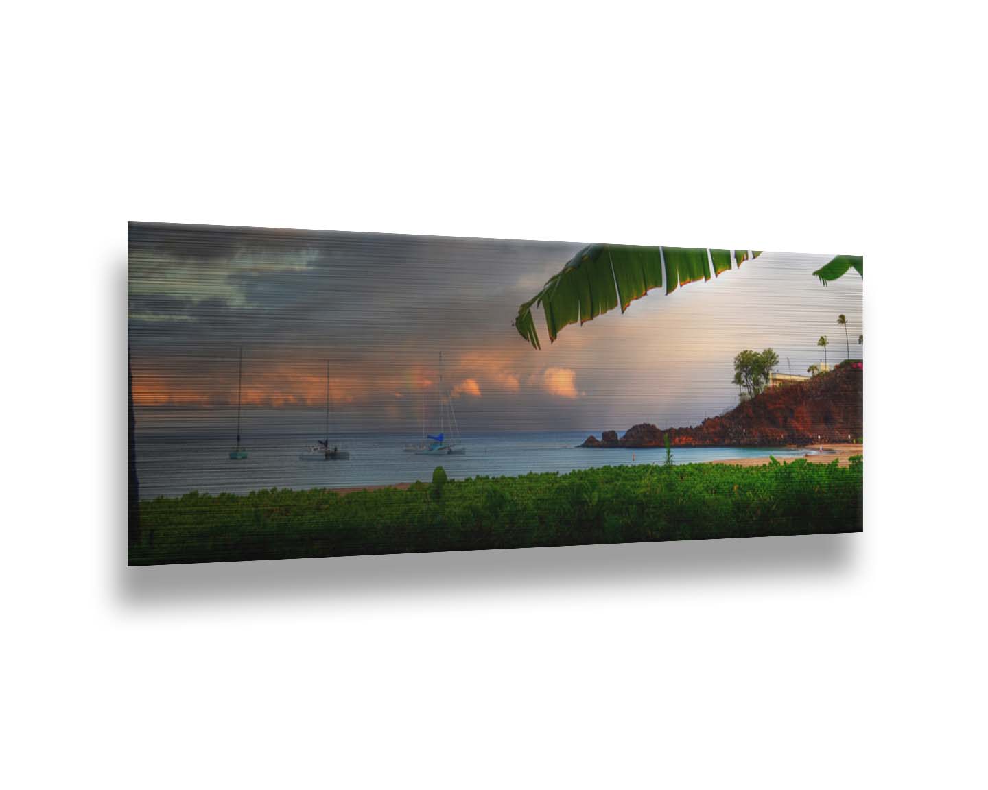 A photograph of Ka'anapali in Maui, Hawai'i. Lush green plants grow on the beach, and sailboats float out on the water. A rainbow pokes down through the clouds before the sunset. Printed on metal.