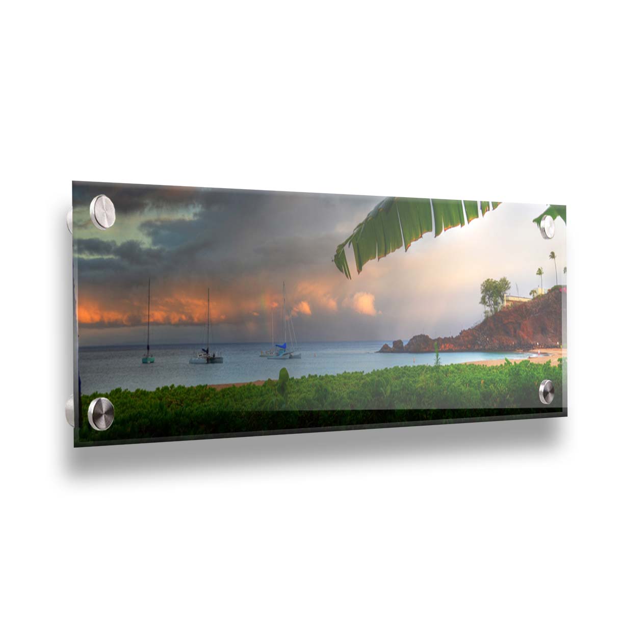 A photograph of Ka'anapali in Maui, Hawai'i. Lush green plants grow on the beach, and sailboats float out on the water. A rainbow pokes down through the clouds before the sunset. Printed on acrylic.