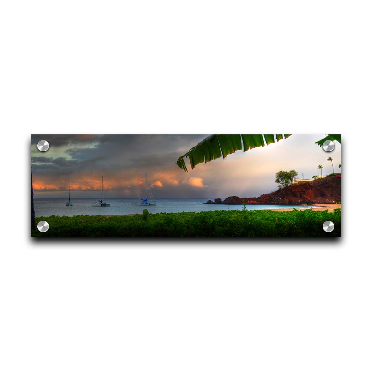 A photograph of Ka'anapali in Maui, Hawai'i. Lush green plants grow on the beach, and sailboats float out on the water. A rainbow pokes down through the clouds before the sunset. Printed on acrylic.