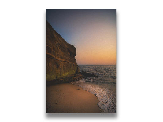 A photograph of La Jolla Cove in San Diego, California at sunset. The warm light reflects on the water, sand, and mossy cliffs. Printed on canvas.